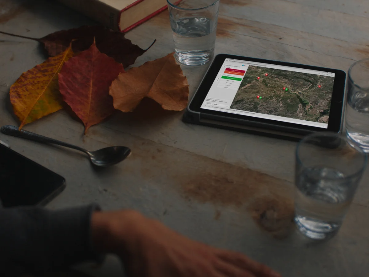 Tablet con mapa de fincas de la red Origen Tu Campo sobre mesa de madera de campo — vista de satélite con pins de productores activos